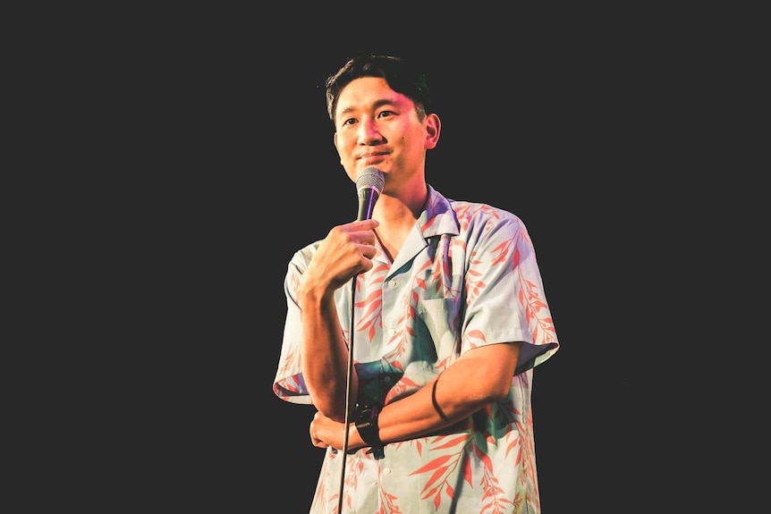 A Japanese man in a colourful shirt, performing stand up comedy