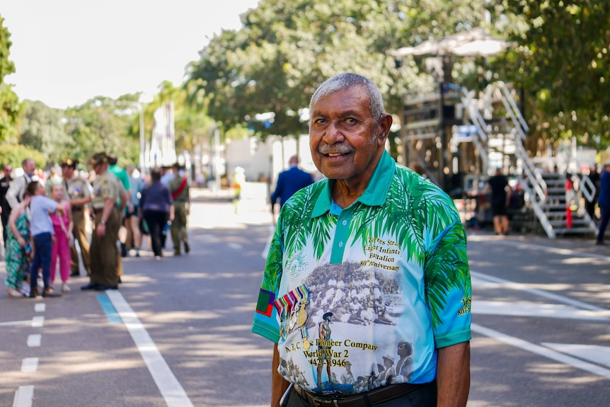 An older man smiles at the camera on Anzac Day at a march.