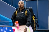 Serena Williams looks up wearing a jacket and bag over her shoulders