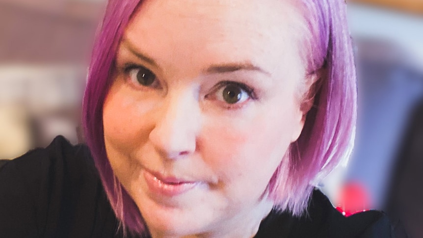 A close up photo of Kate Stone Matheson, who has pink hair and is wearing a black top
