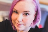 A close up photo of Kate Stone Matheson, who has pink hair and is wearing a black top