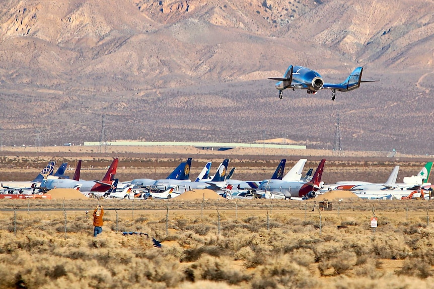 A spacecraft comes into landing next to aircraft on a desert airstrip.