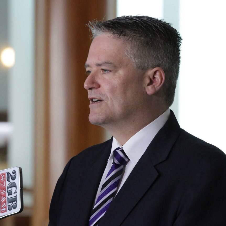 Senator Cormann looks left of frame, and is mid sentence. He's wearing a purple, black and silver tie.