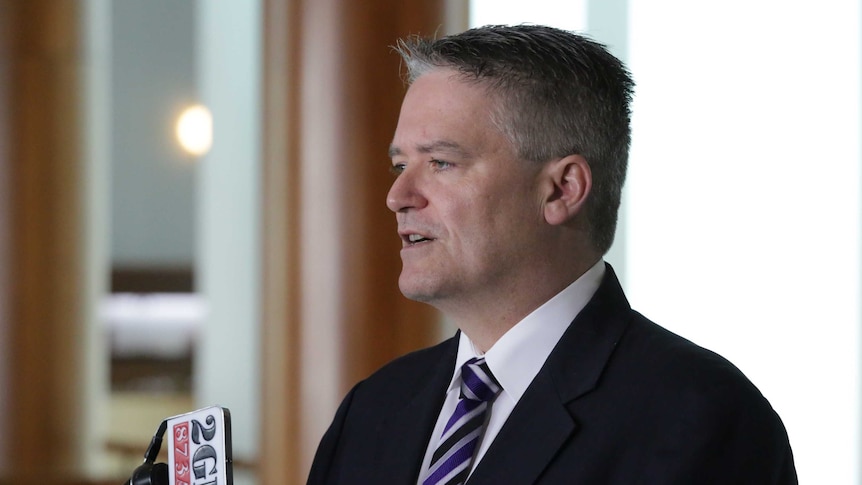 Senator Cormann looks left of frame, and is mid sentence. He's wearing a purple, black and silver tie.