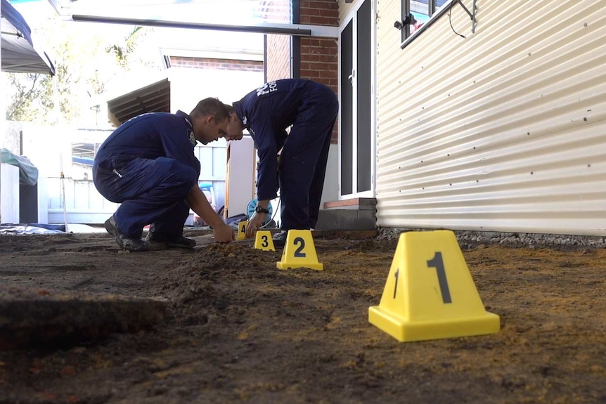 Forensic police lay yellow evidence markers in an excavated section of a backyard.