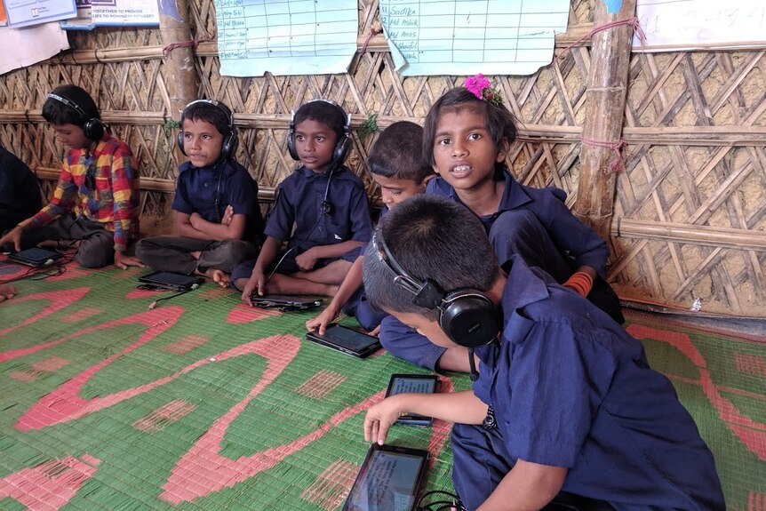 Children play with tablet computers in a learning centre. They wear navy blue uniforms.