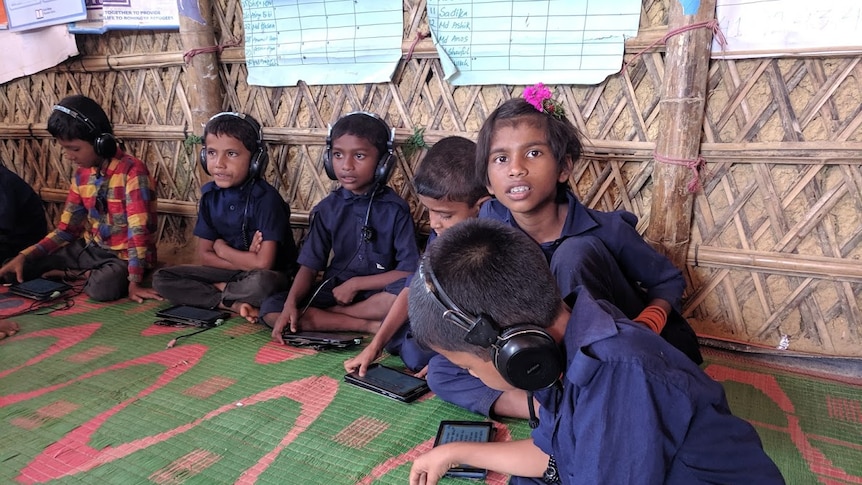 Children play with tablet computers in a learning centre. They wear navy blue uniforms.