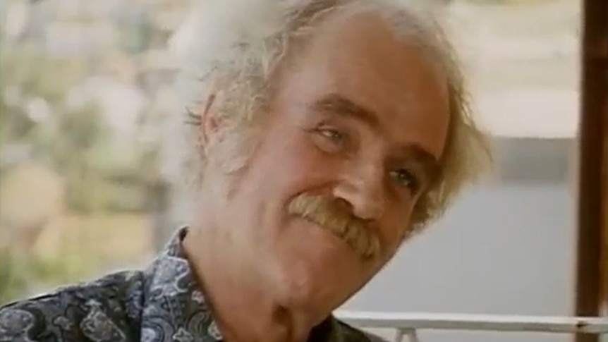 A 1970s TV still of an older, balding man with a moustache and wiry eyebrows