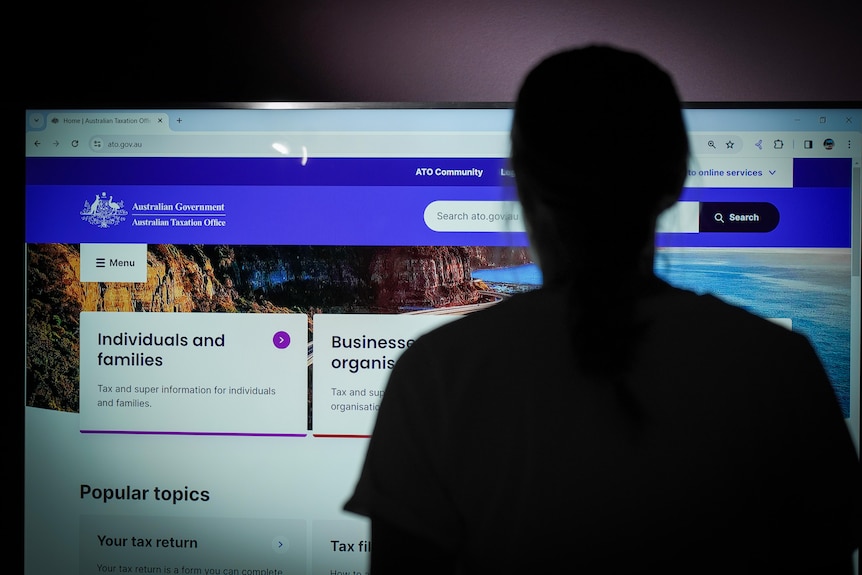 Una figura oscurecida de una persona parada frente al sitio web de la ATO en una pantalla.