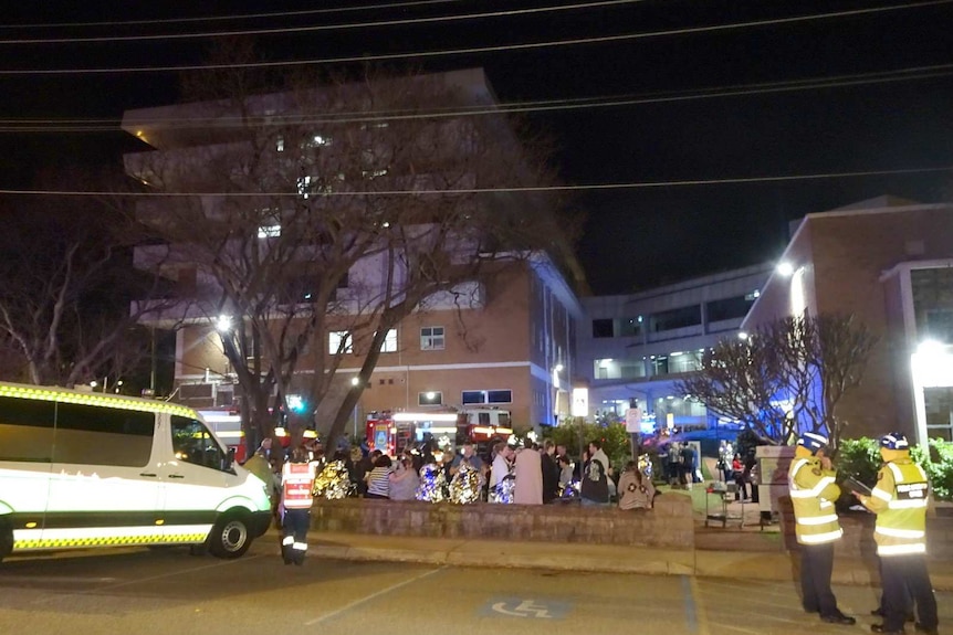 Patients, an ambulance and firefighters outside St John of God Hospital at night.