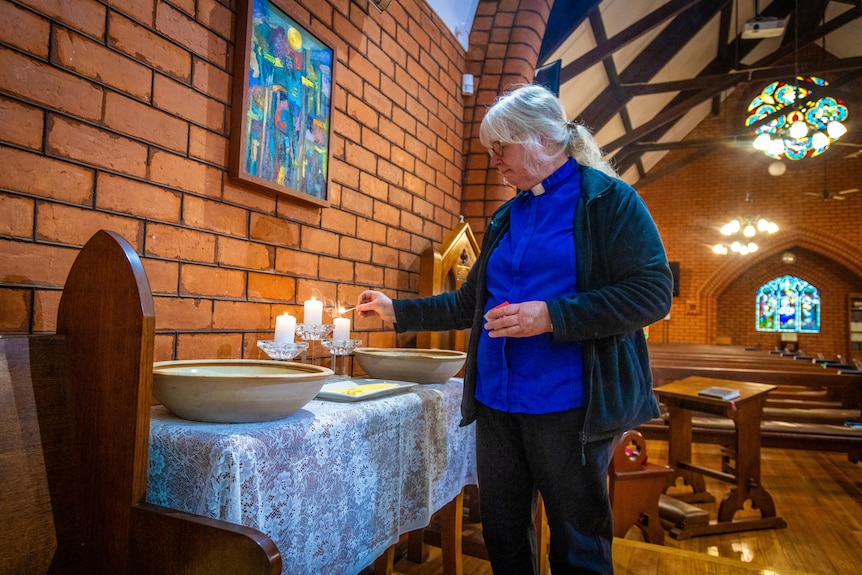 Woman in clerical clothing lights candles in a church