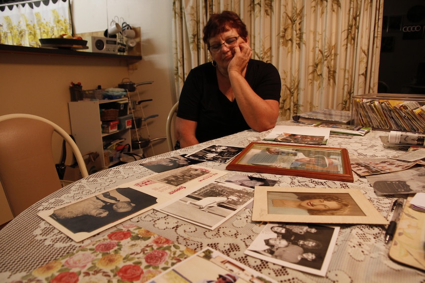 Woman sitting at a table with old photos sprawled out in front of her.