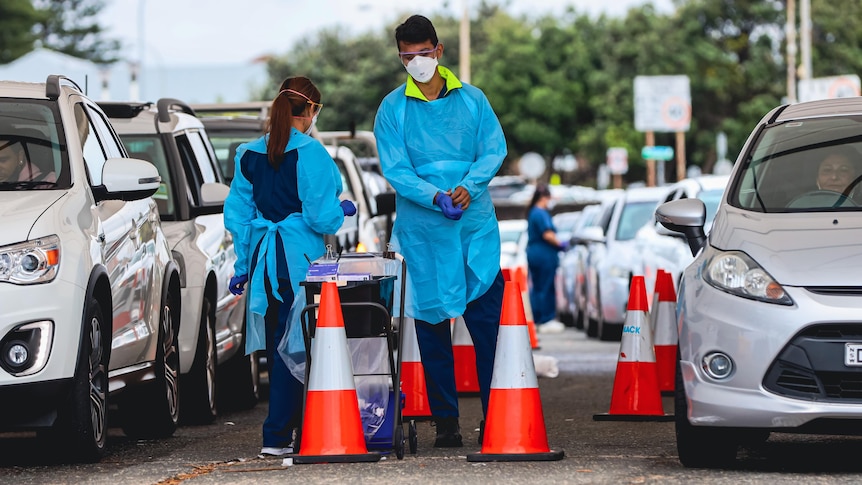 A man and a woman wearing masks administer COVID tests