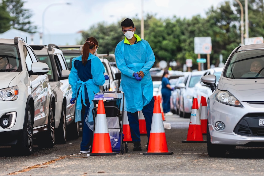 A man and a woman wearing masks administer COVID tests