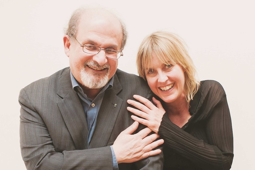 Salman Rushdie and Caro Llewellyn in a friendly pose with their hands on each others' shoulders.
