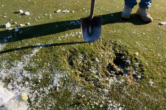 A shovel tip near the area where ice fell on a golf course, with ice visible near the edge of the frame.