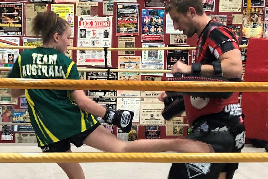 Girl with Team Australia shirt in boxing ring kicks at a man dressed with pads