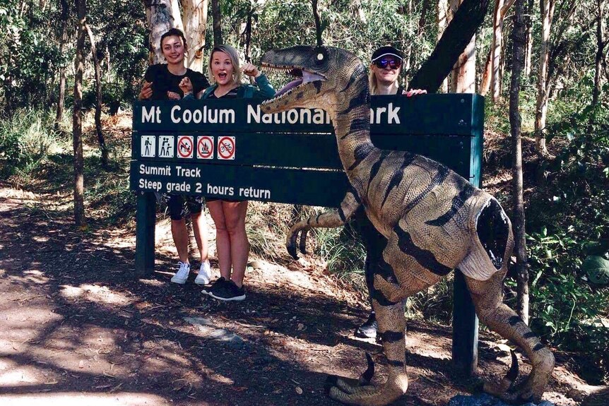 three women stand with the dinosaur at entrance to the national park