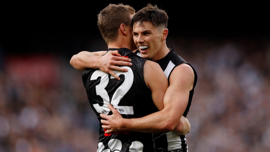 Two Collingwood AFL players embrace as they celebrate a goal against Carlton.