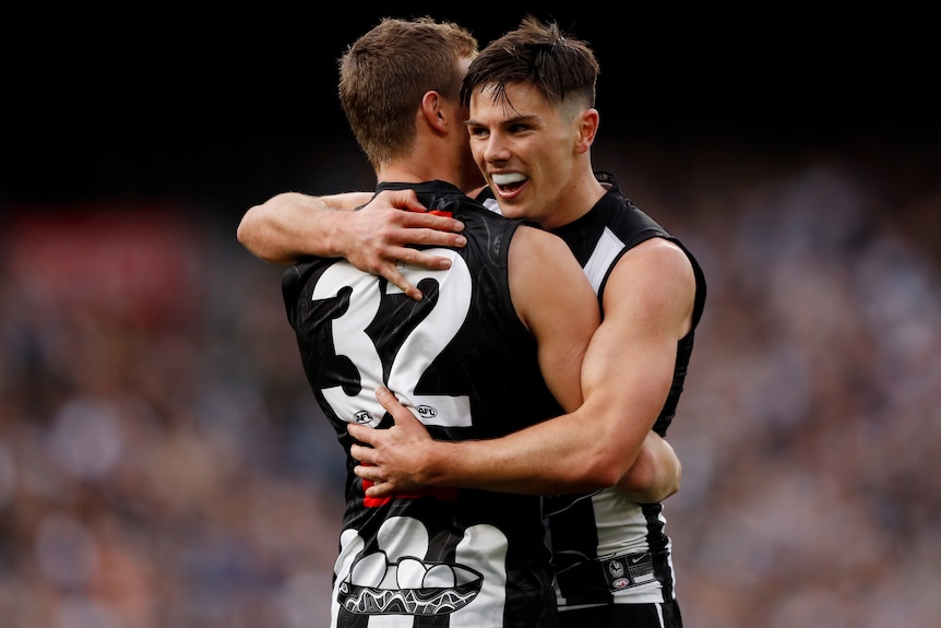 Two Collingwood AFL players embrace as they celebrate a goal against Carlton.