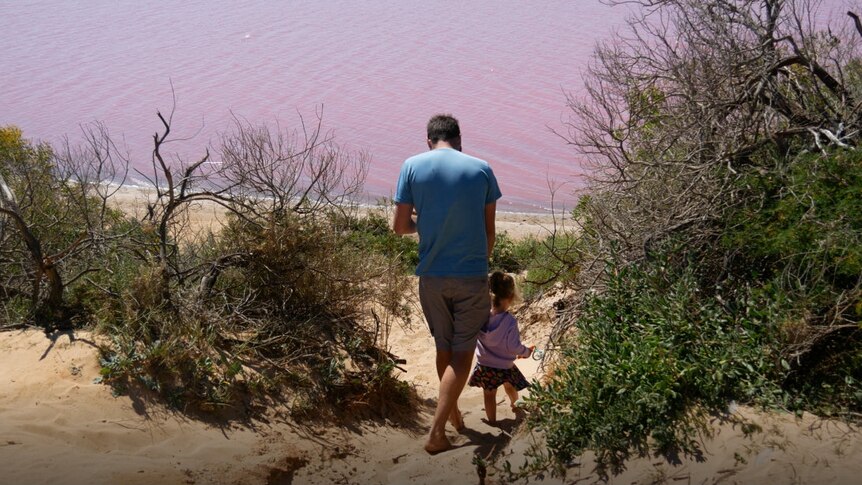 Man and his child walking through scrub to reach the edge of the pink lake