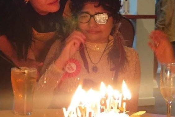 Жена с очила плаче над торта за рожден ден, заобиколена от семейството си.