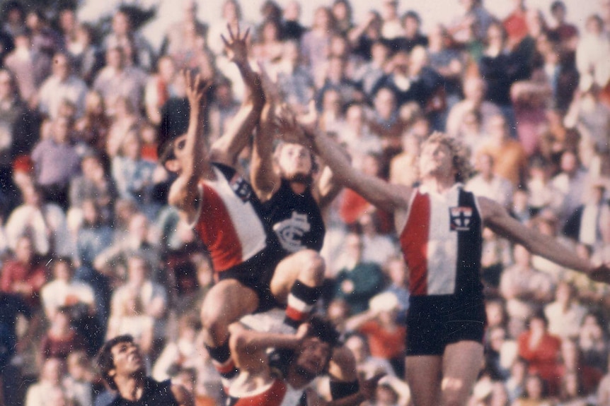 Football players leap over each other for the ball in an Australian football game.