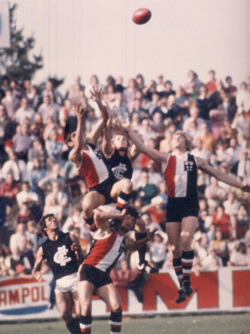 Football players leap over each other for the ball in an Australian football game.