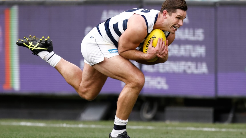 A young man in a white and black AFL jersey strains to catch a yellow ball.