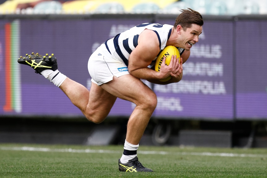 A young man in a white and black AFL jersey strains to catch a yellow ball.