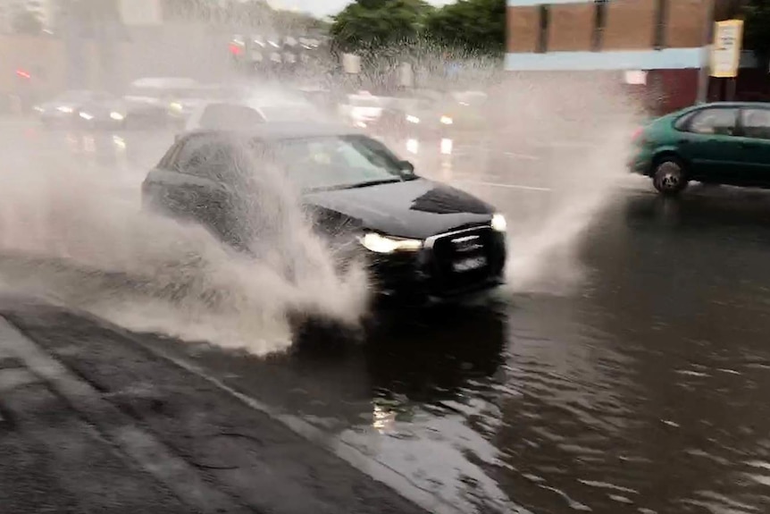 Car sprays up water as it drives on road during storm in Brisbane on October 21, 2018