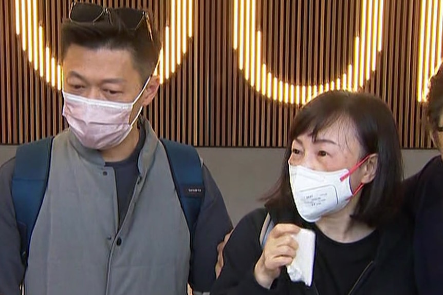 A man and a woman wearing face masks and looking emotional at the airport.