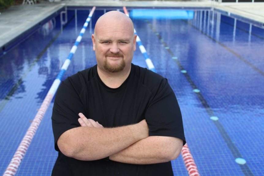 A man stands in front of a lap pool which is a deep blue colour