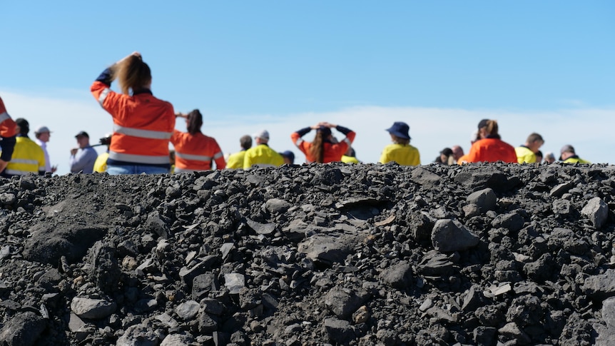 Coal rocks in the foreground with people in the background standing in high vis