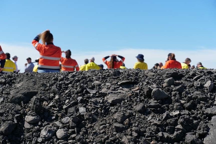 Coal rocks in the foreground with people in the background standing in high vis