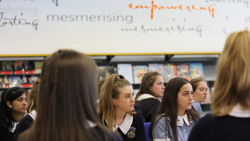 Female high school students sit in a library. On the wall behind them the word empowering is highlighted.