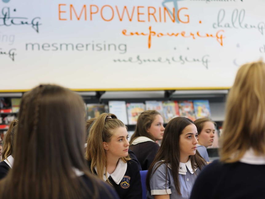 Female high school students sit in a library. On the wall behind them the word empowering is highlighted.