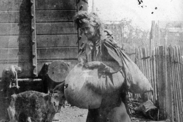 Historical photograph of Annie Ferdinand, also known as Annie Bags, she is dressed in rags and accompanied by an emaciated dog.