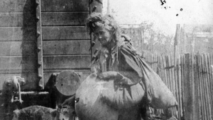 Historical photograph of Annie Ferdinand, also known as Annie Bags, she is dressed in rags and accompanied by an emaciated dog.
