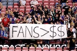 Spectators hold a sign in protest during the round eight A-League Men's match between Newcastle Jets and Brisbane Roar.