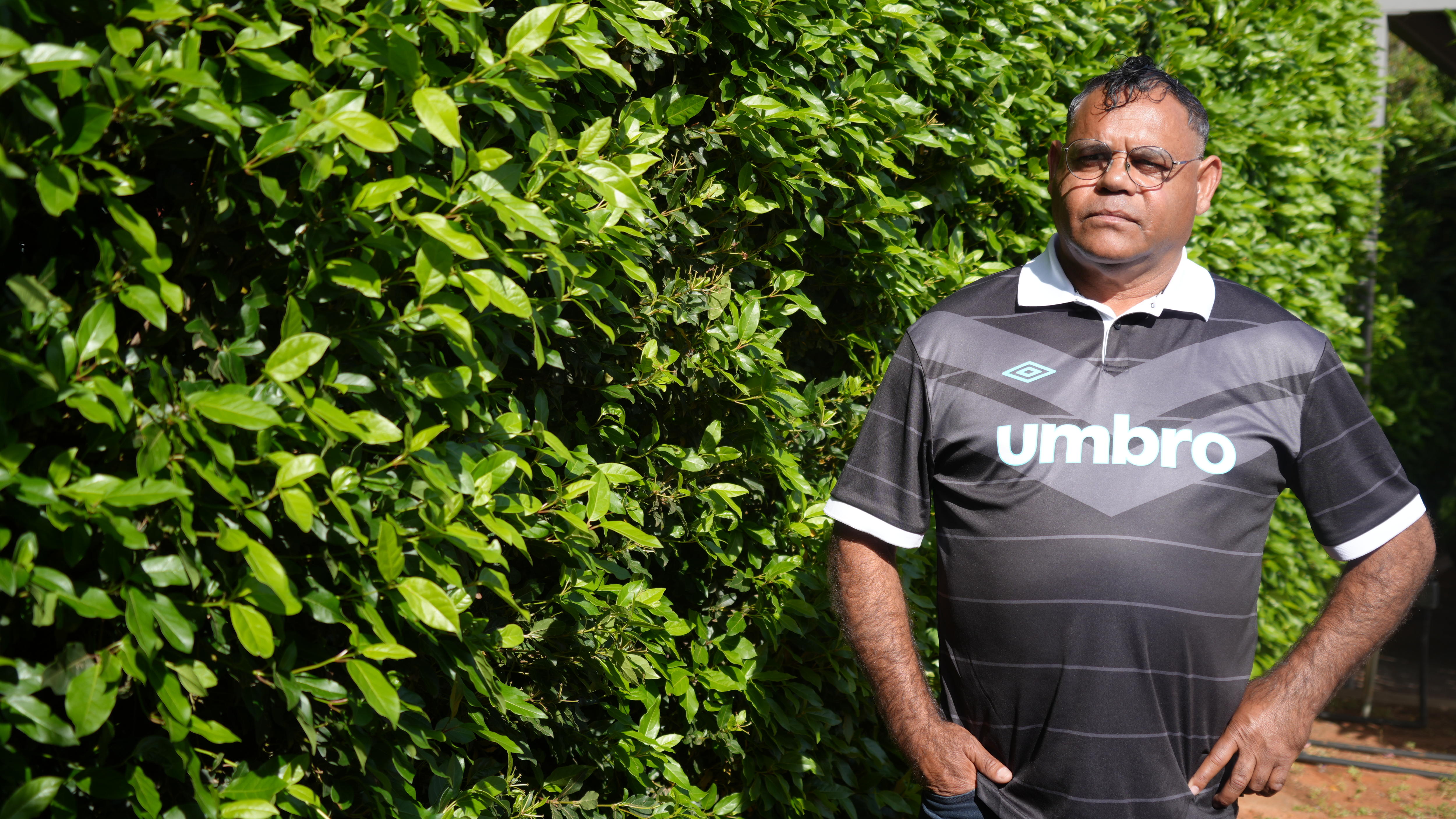 Owen Whyman standing looking past camera in front of bushes