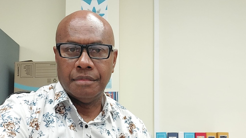 Neville Devete wears a floral collared shirt and looks seriously at the camera in an office.