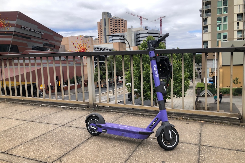 A purple e-scooter parked on a bridge overlooking tall buildings