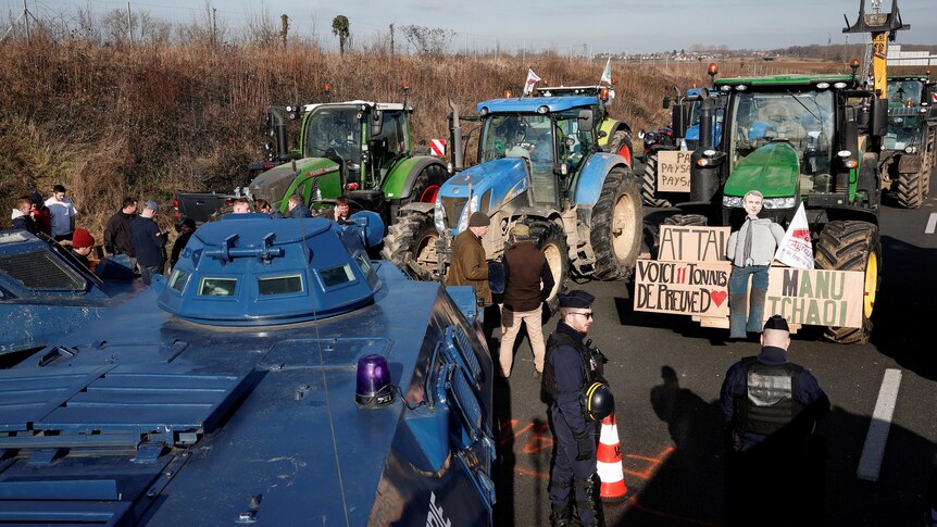 Blue tractors and green tractors face one another on a highway.