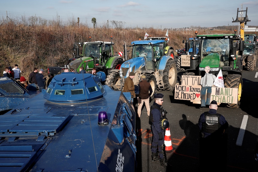 Blue tractors and green tractors face one another on a highway.