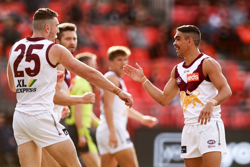 Two AFL players reach palms and elbows toward each other in celebration of a goal.