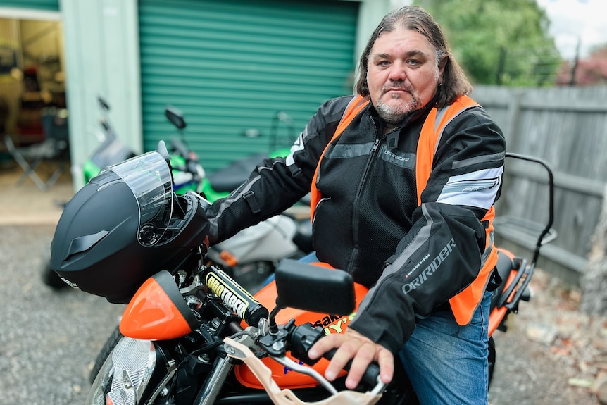 A man in motorcycle leathers sits on a bike.