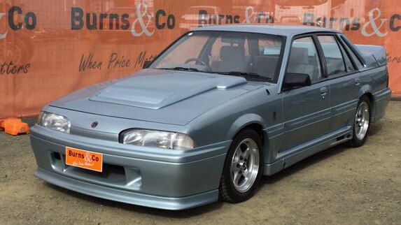 A boxy 1988 VL Walkinshaw Group Commodore in Panorama Silver parked at an auction lot.