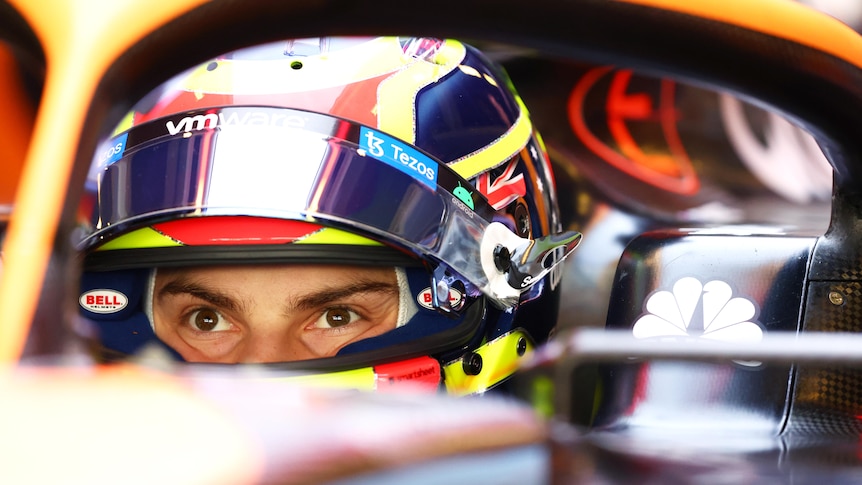 Australian F1 driver Oscar Piastri sits in his McLaren car with helmet on and eyes wide before his first test drive.