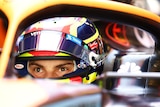 Australian F1 driver Oscar Piastri sits in his McLaren car with helmet on and eyes wide before his first test drive.
